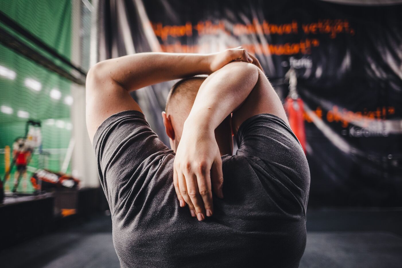 Man seen from behind stretching one arm over his head in a sports hall