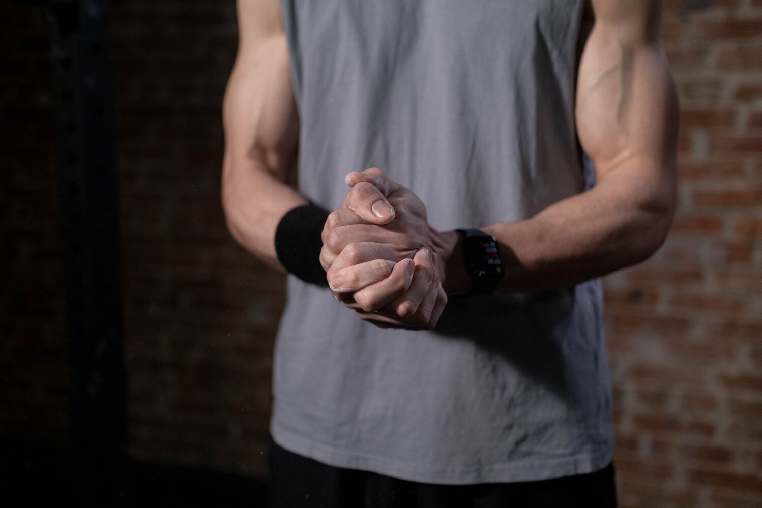 Person in a sleeveless grey shirt loosely clasping both hands in front of the body